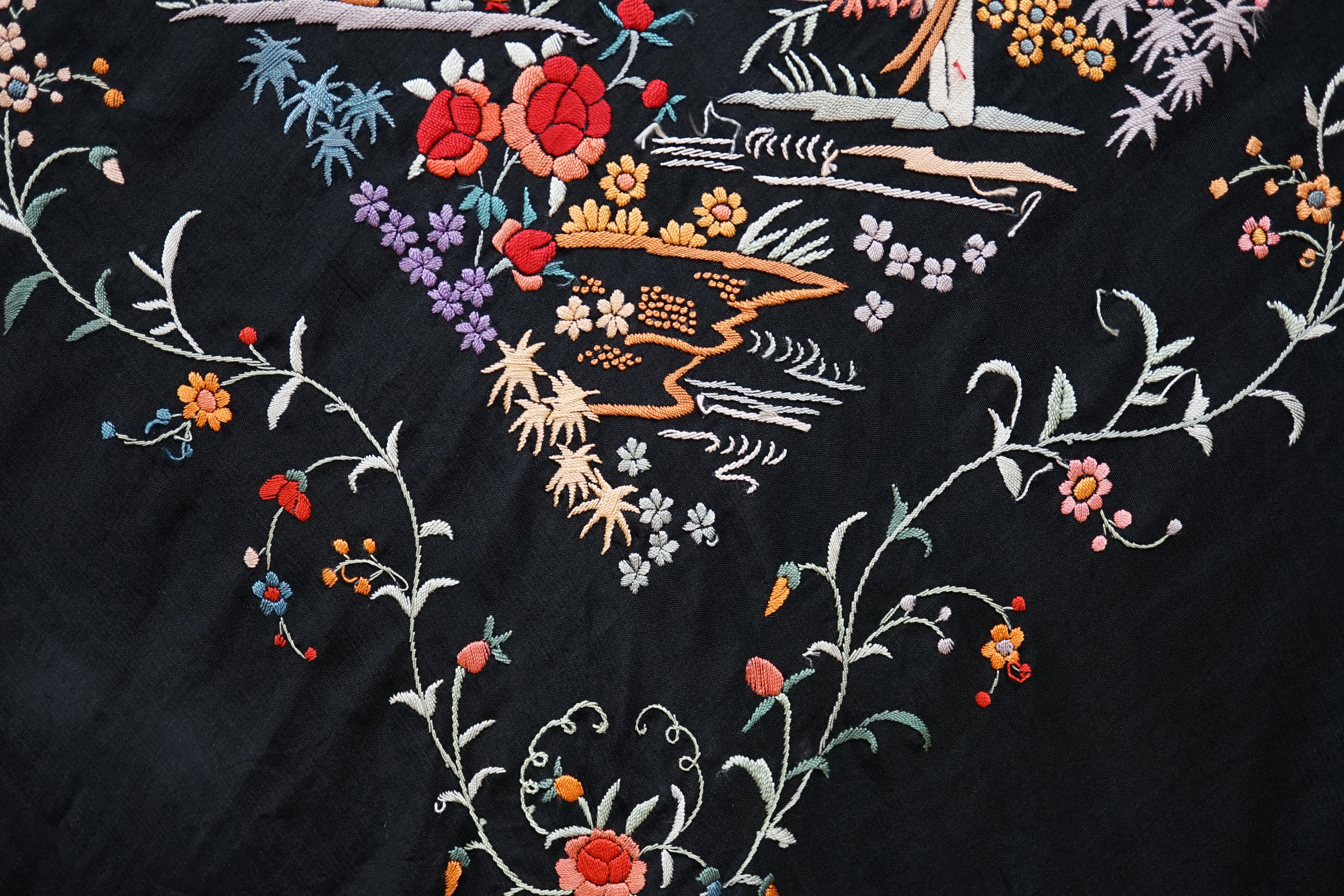 An early 20th century Chinese black silk shawl, with all over coloured floral embroidery, embroidered with multi-coloured silks and a long silk fringe, unusually the four corners are embroidered with a figurative pagoda